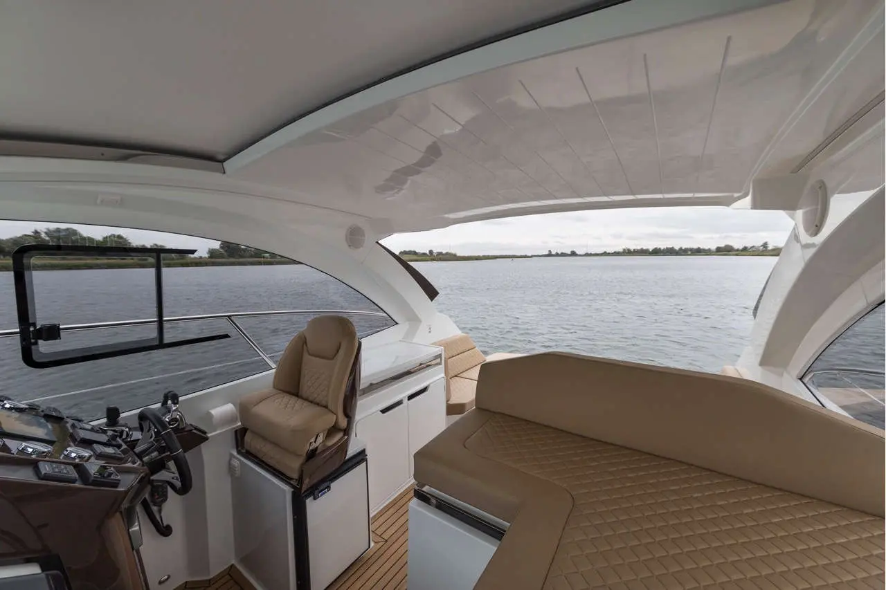 Interior of a luxury motorboat with plush seating, navigating a calm waterway under a cloudy sky.