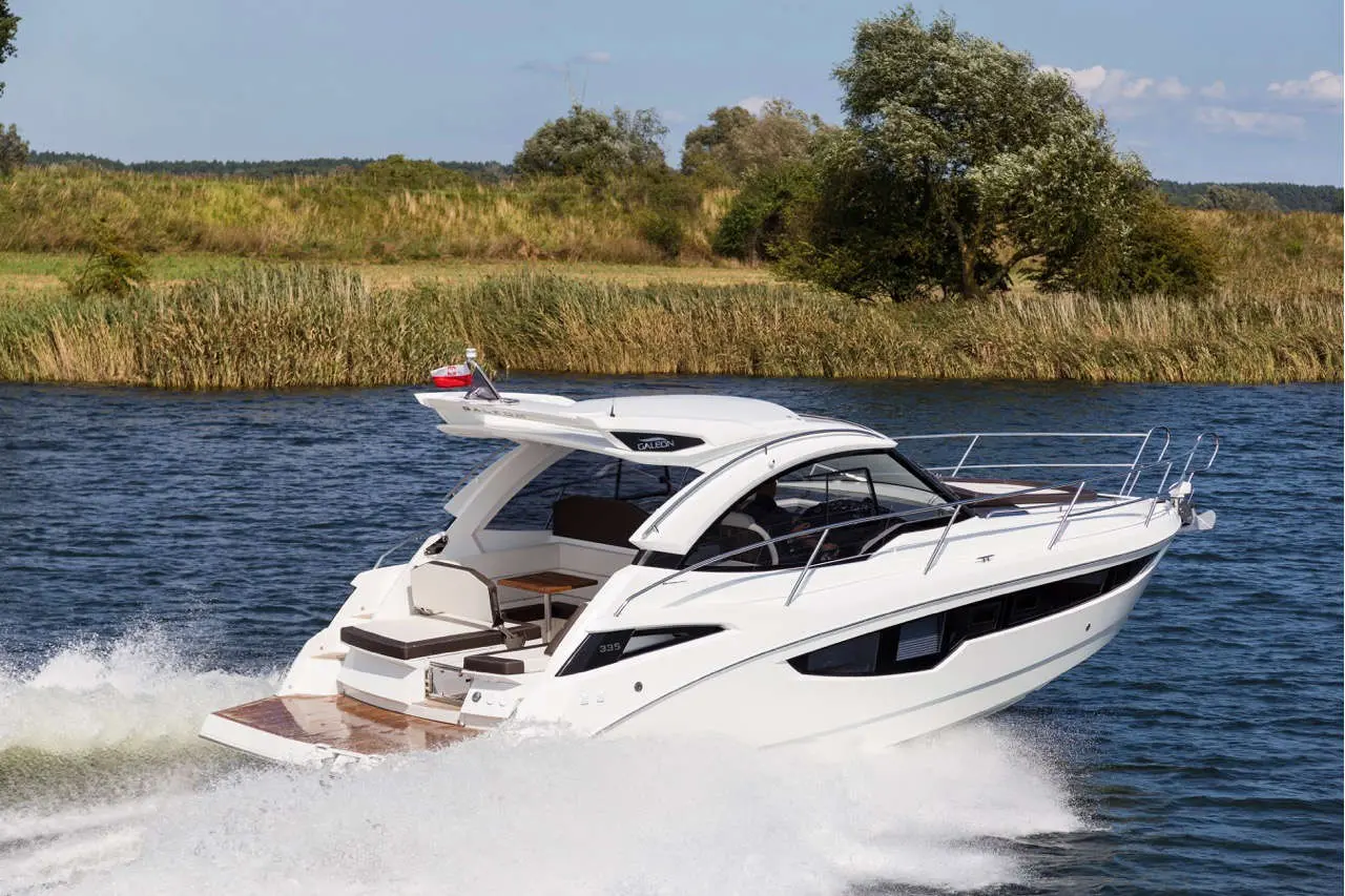 A sleek white motorboat speeds through a calm river with lush greenery in the background, creating a wake of water.