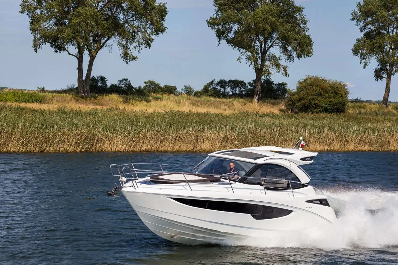 A white motorboat speeds across a river with trees and grassland in the background, highlighting recreational boating.
