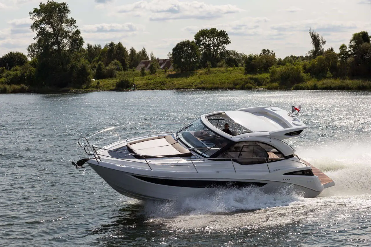 A sleek motorboat navigates a shimmering river, with a driver at the helm. Lush greenery lines the shore.