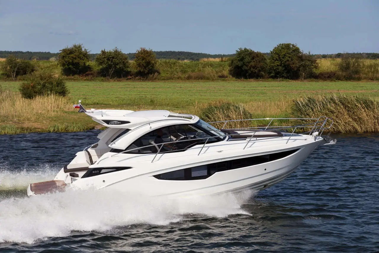 Luxury white motorboat gliding on water, showcasing sleek design amidst lush green landscape with distant trees.