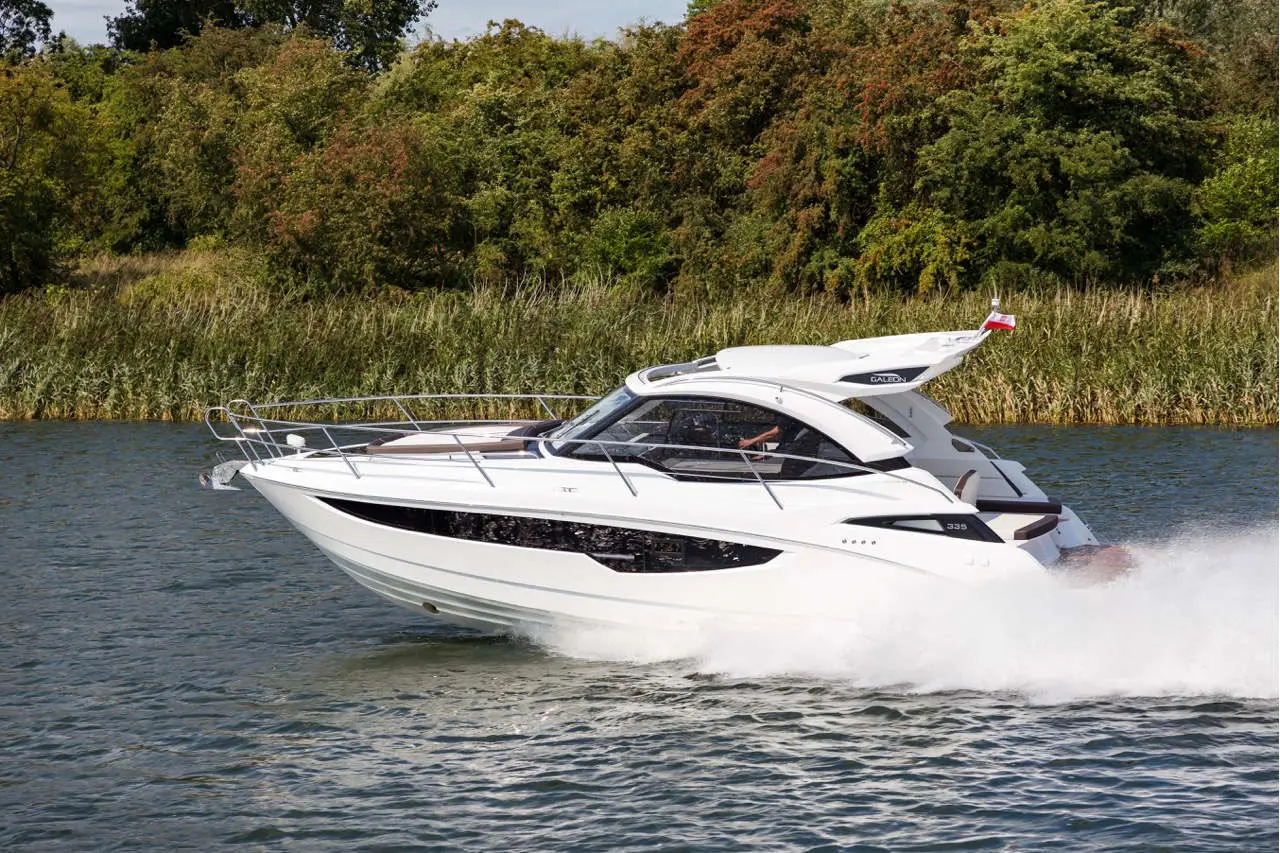 White motor yacht cruising in a calm waterway, with green foliage in the background and a Polish flag at the stern.