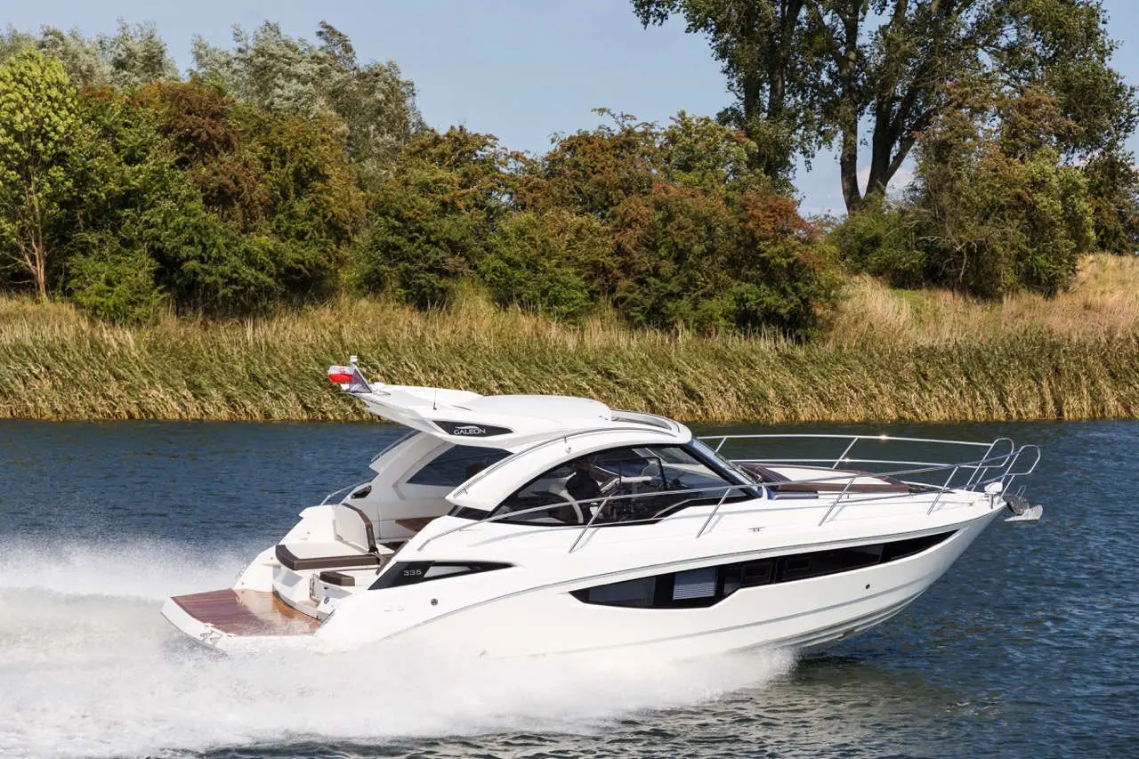 A sleek white motorboat, model Galeon 335, gliding over water with lush greenery in the background.