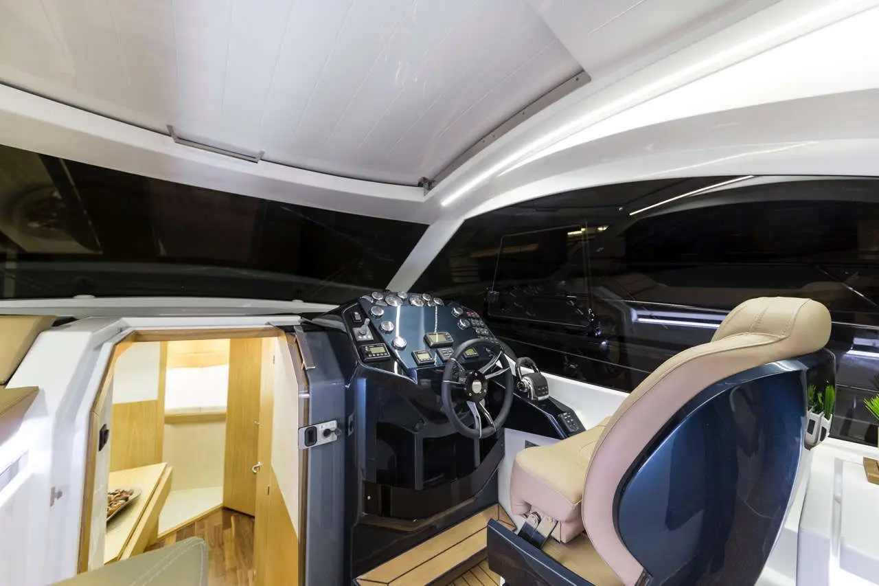 Modern boat cockpit featuring steering wheel, controls, and plush seating, with a view into the cabin area.