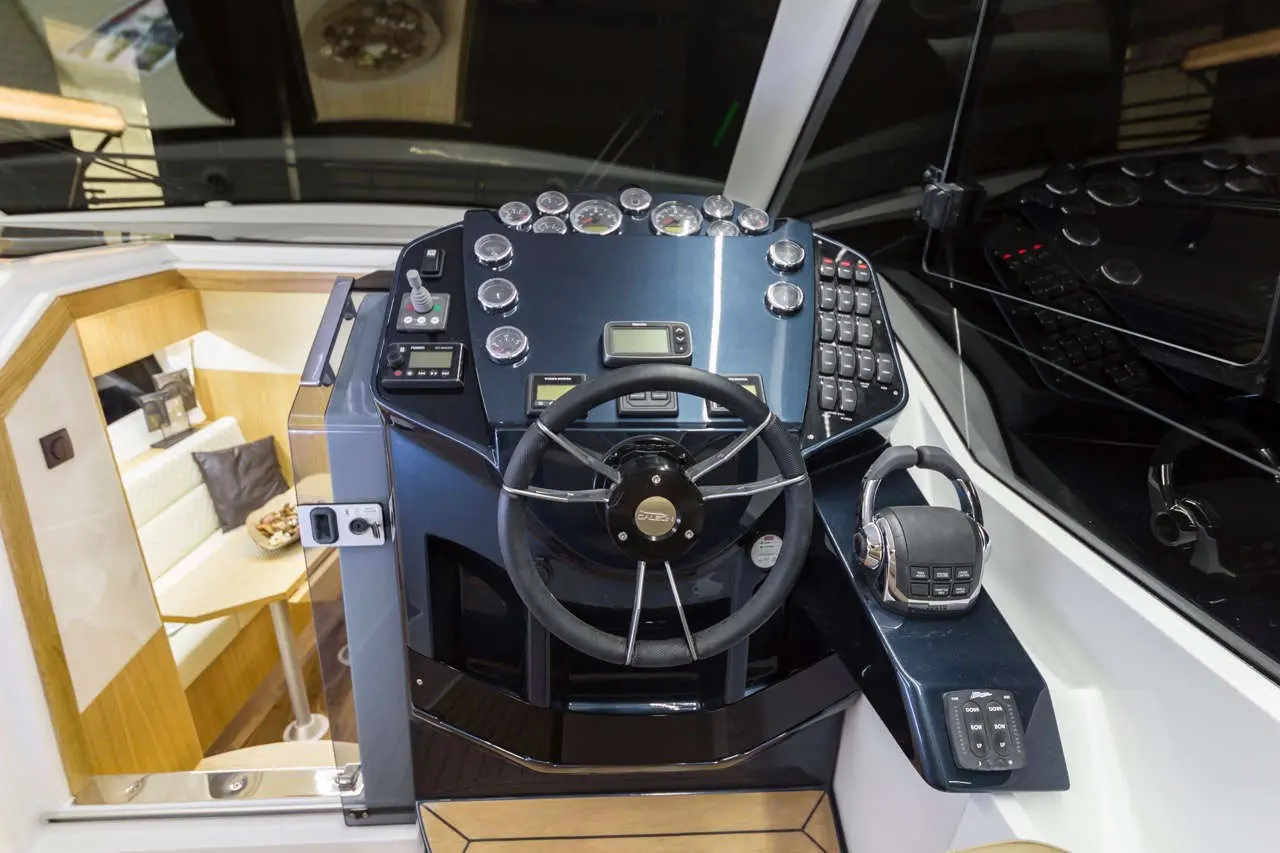 Boat steering console featuring a wheel, gauges, buttons, and a control panel with a radio, in a sleek modern design.