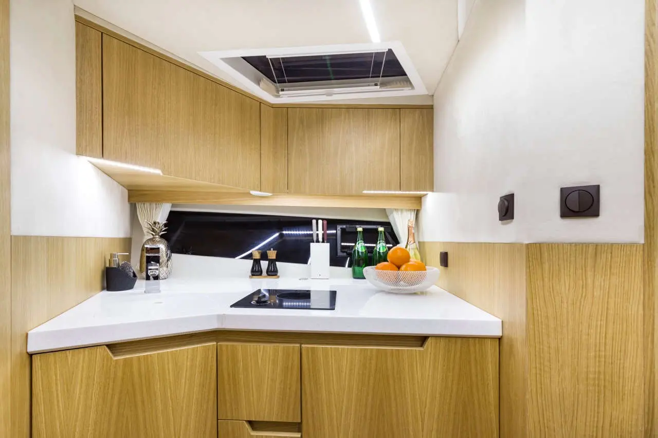 Modern kitchen with wood cabinets, white countertop, cooking area, green bottles, and a bowl of oranges on display.