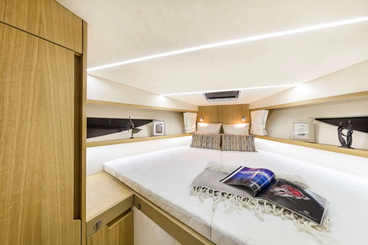 Cozy boat cabin featuring a double bed, decorative pillows, and a book on a bedside table, all with warm lighting.