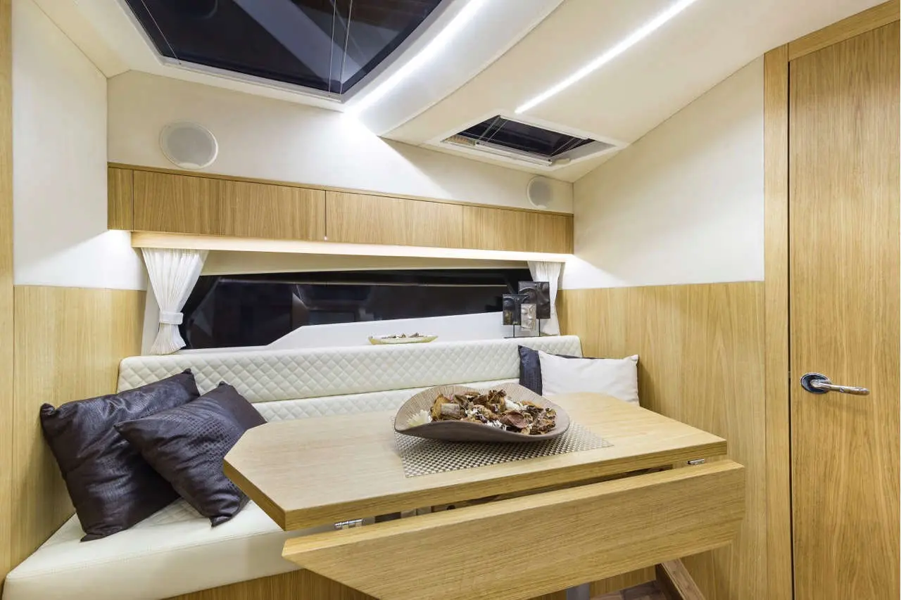Modern yacht interior featuring a cozy dining area with cream cushions, decorative pillows, and a centerpiece of snacks.