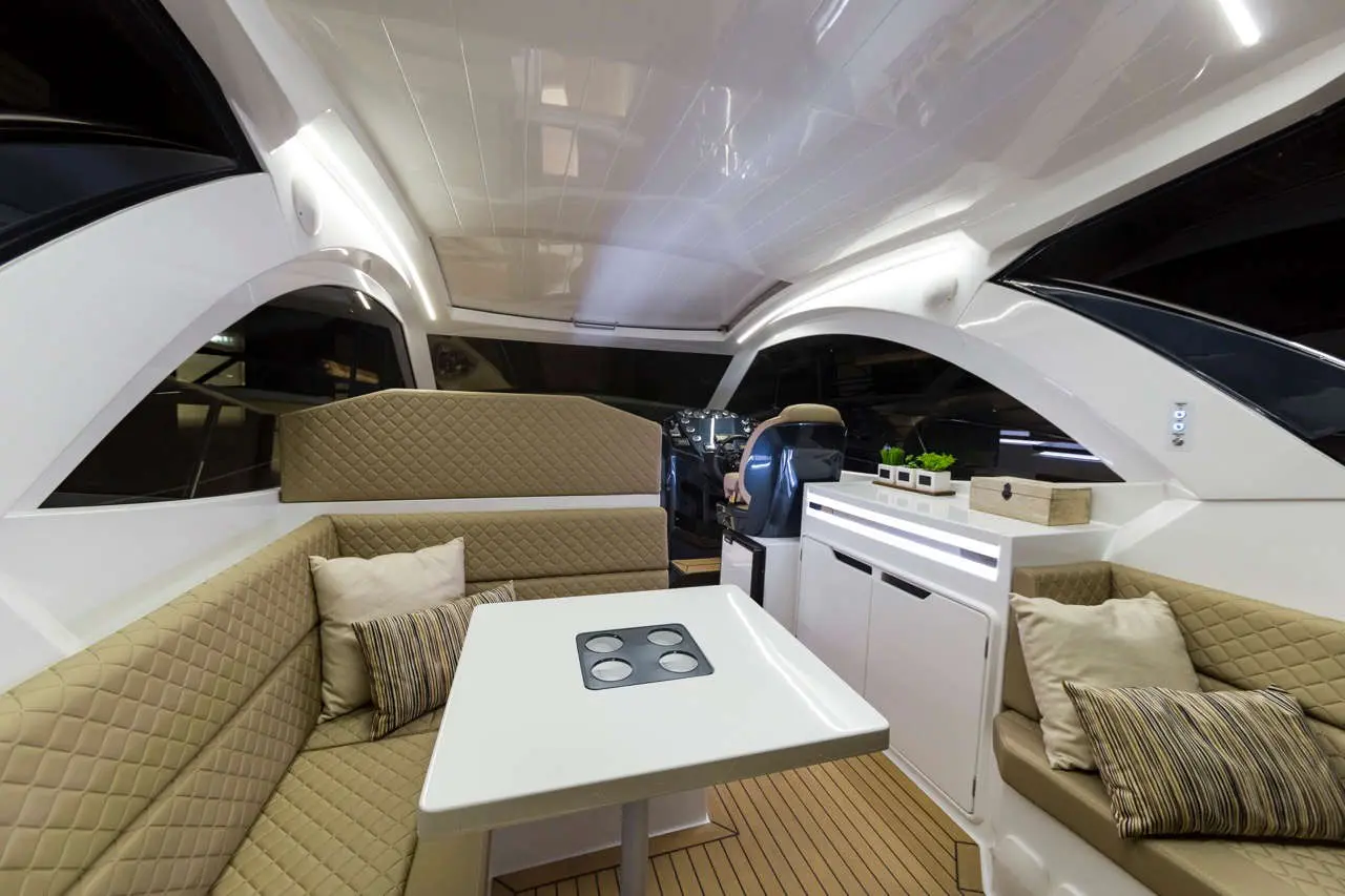 Interior of a modern yacht featuring a white table, upholstered seating, and a sleek dashboard with plants on a counter.