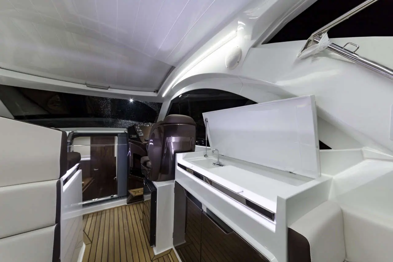 Interior of a modern boat, featuring a helm chair, storage area, sink, and wooden flooring, illuminated in soft lighting.