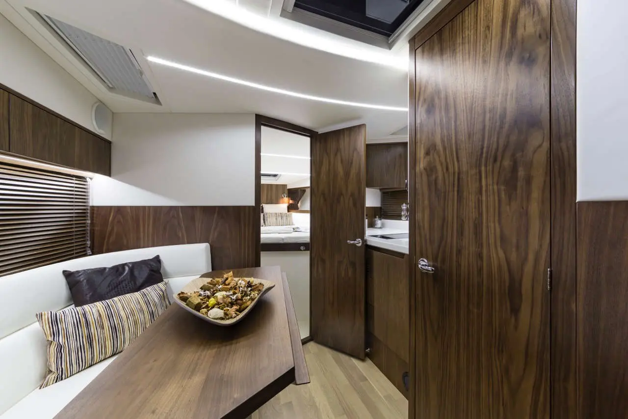 Modern yacht interior featuring wood finishes, a dining area, and an open doorway to the kitchen space.