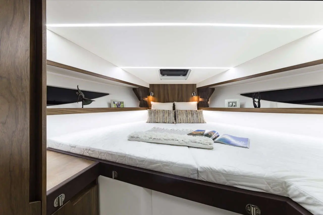 Cozy yacht bedroom featuring a large bed, striped pillows, reading lights, and decorative items on shelves.