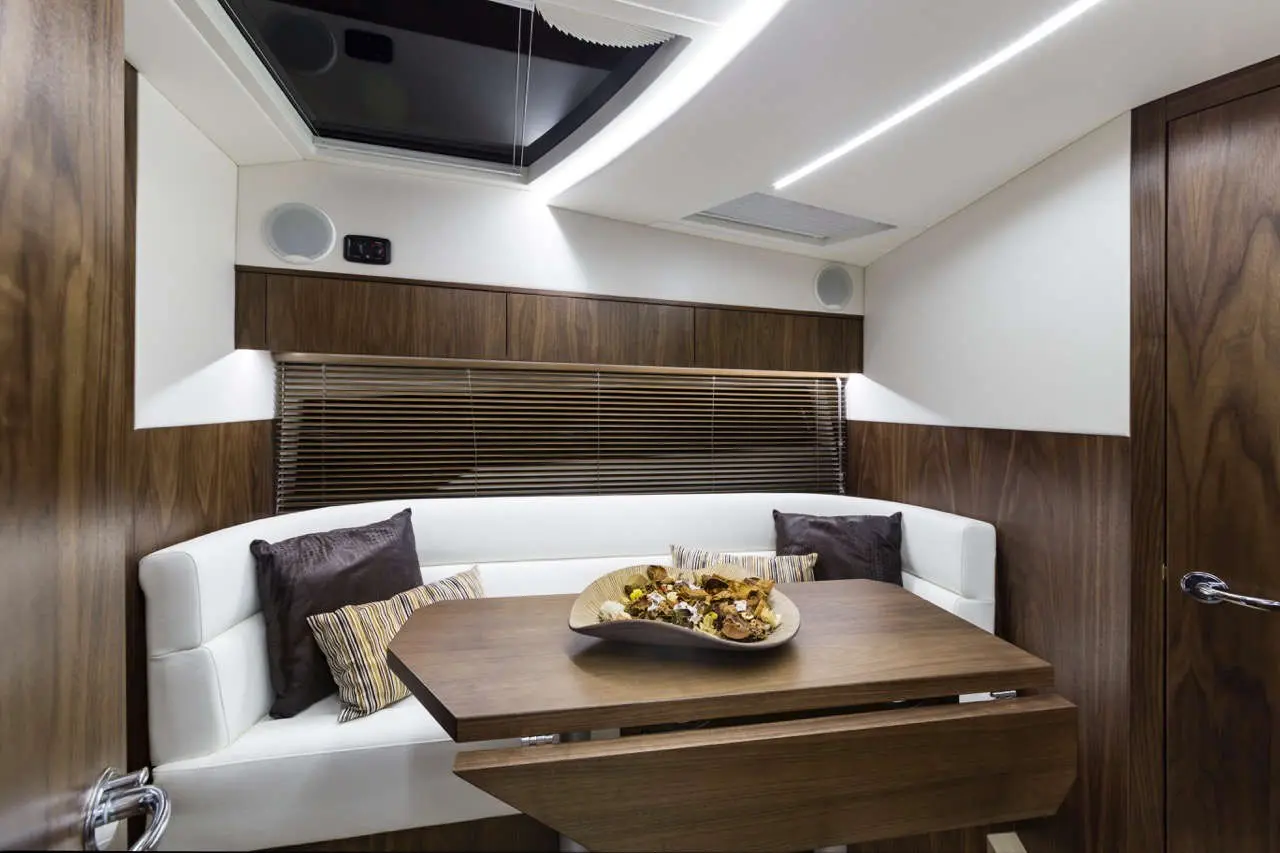 Modern boat interior featuring a comfortable seating area, wooden dining table, and a bowl of snacks against a light backdrop.