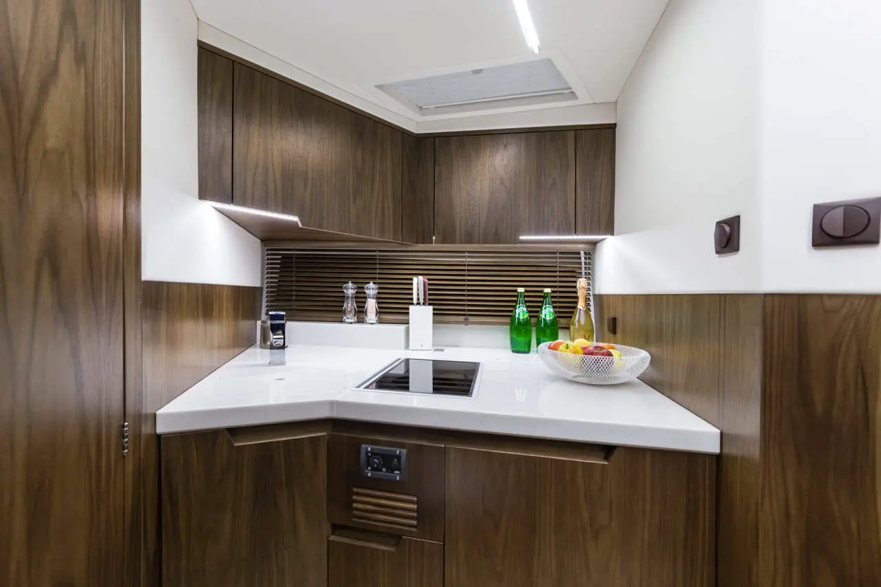 Modern kitchen with dark wooden cabinetry, white countertop, bottles of sparkling water, and a fruit bowl with apples.