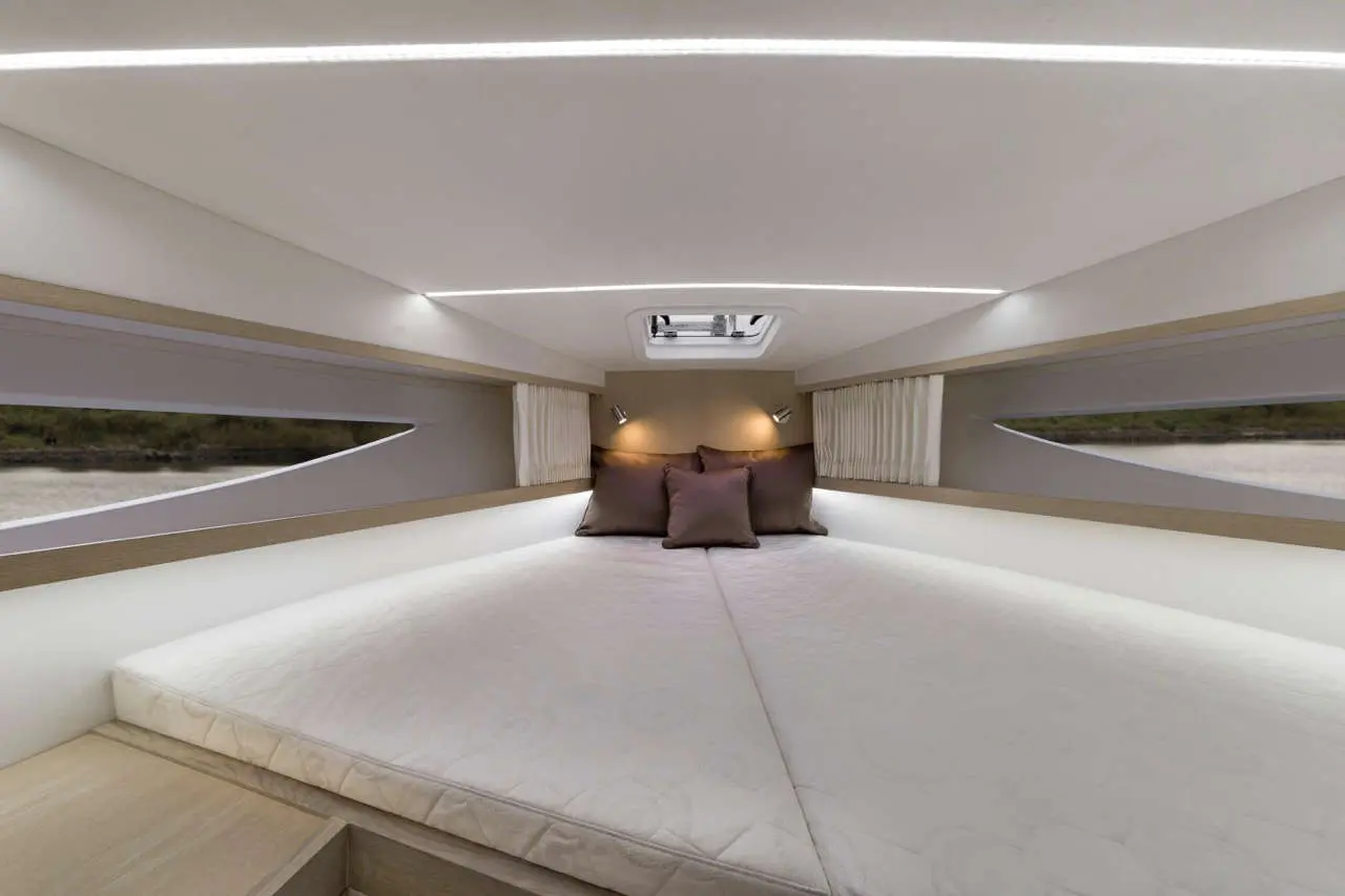 Modern cabin interior featuring a spacious bed with cushions, ambient lighting, and large windows for natural light.