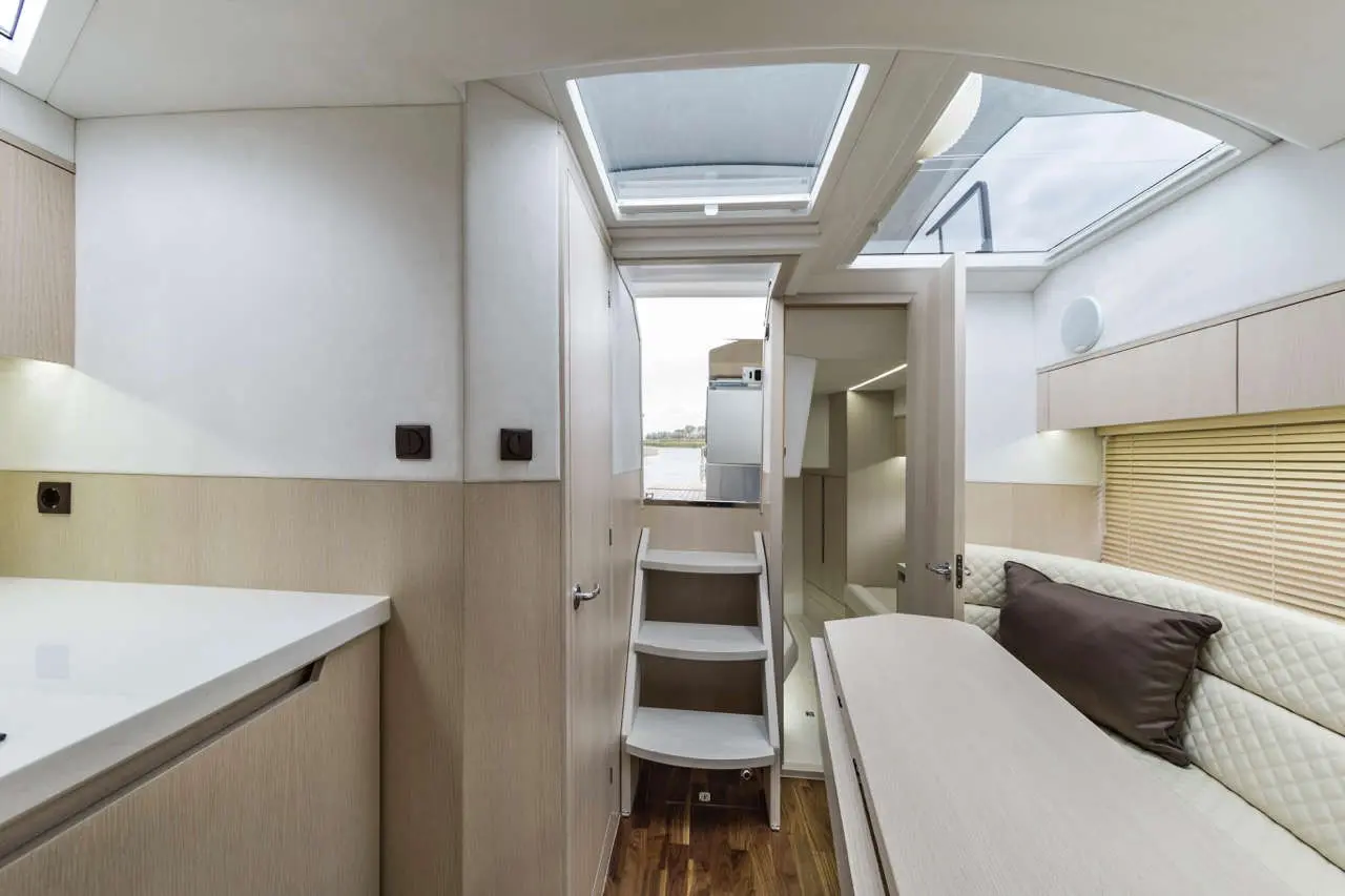 Interior of a modern boat cabin featuring skylights, wooden flooring, stairs, a sofa, and storage space.