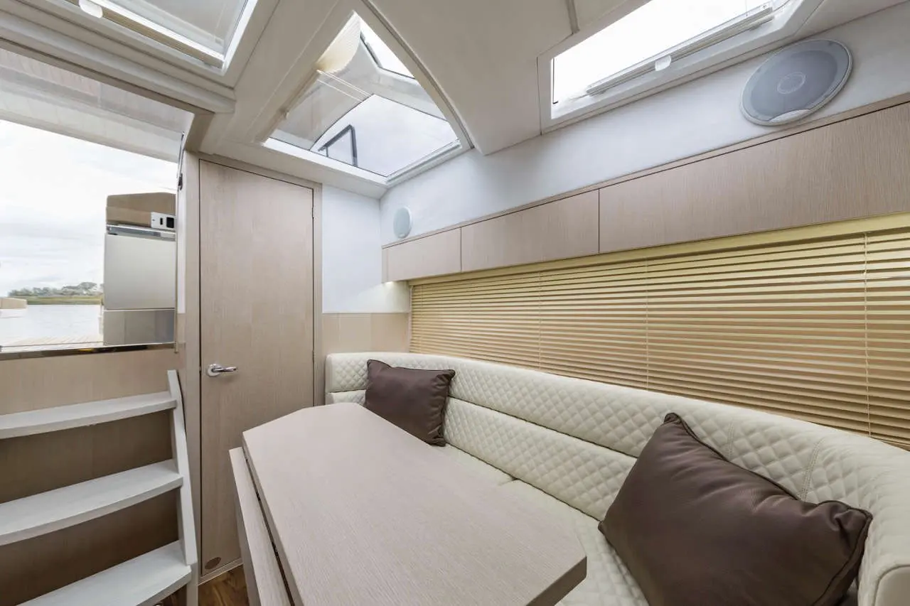 Interior of a modern boat cabin featuring a cream-colored sofa with cushions, a wooden table, and large windows for natural light.