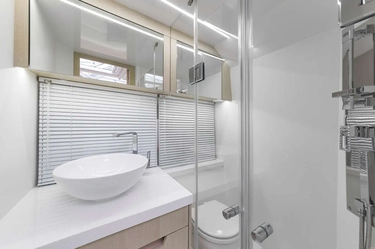 Modern bathroom featuring a white basin, mirror cabinet, shower enclosure, and a toilet beside window blinds.