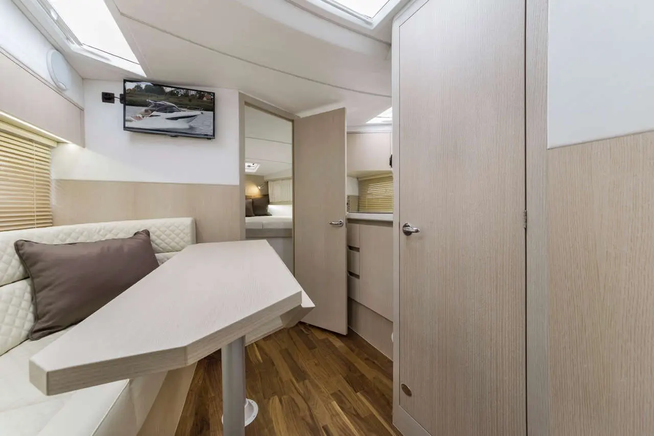 Modern yacht interior featuring a dining area, kitchenette, and a TV displaying a boat image, with sleek wooden flooring.