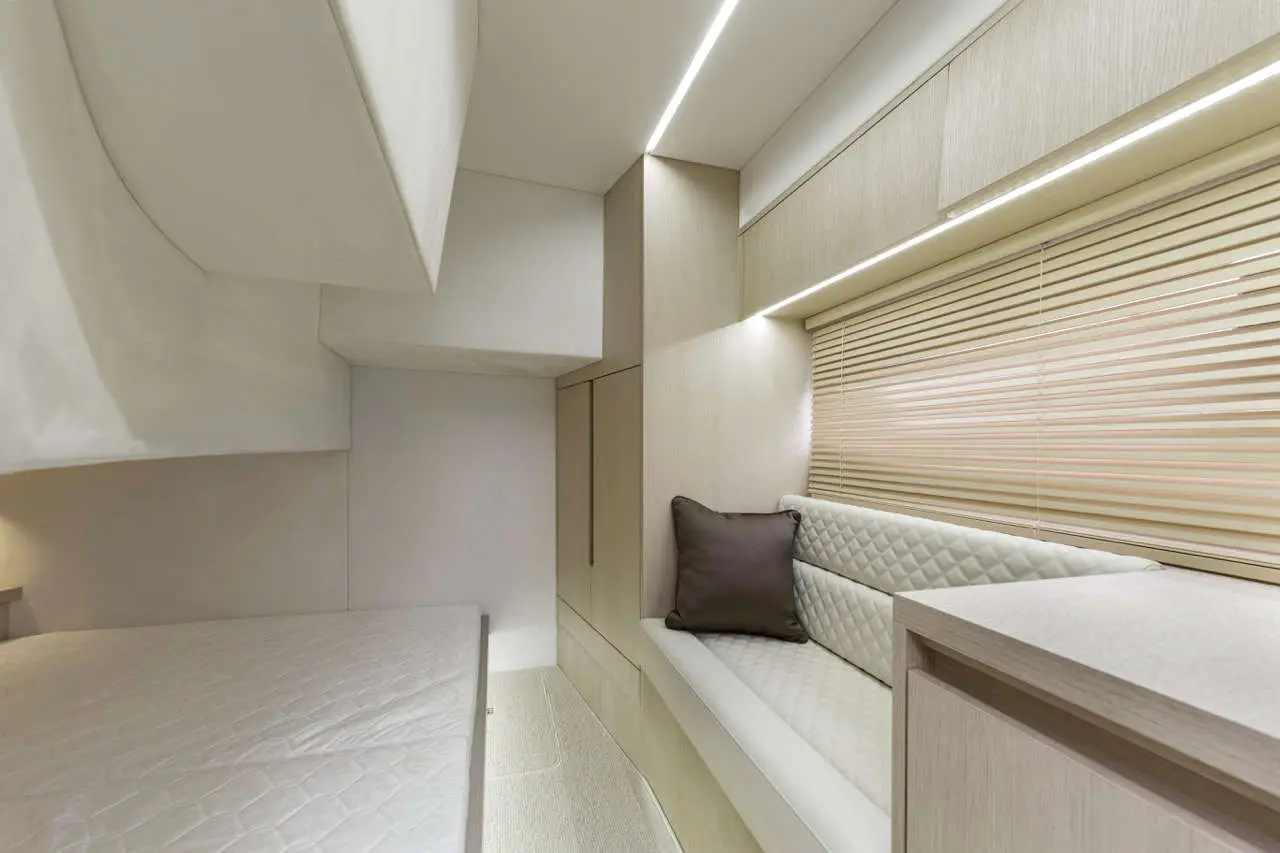 Modern compact bedroom featuring a double bed, soft seating area, and integrated storage, with warm ambient lighting.