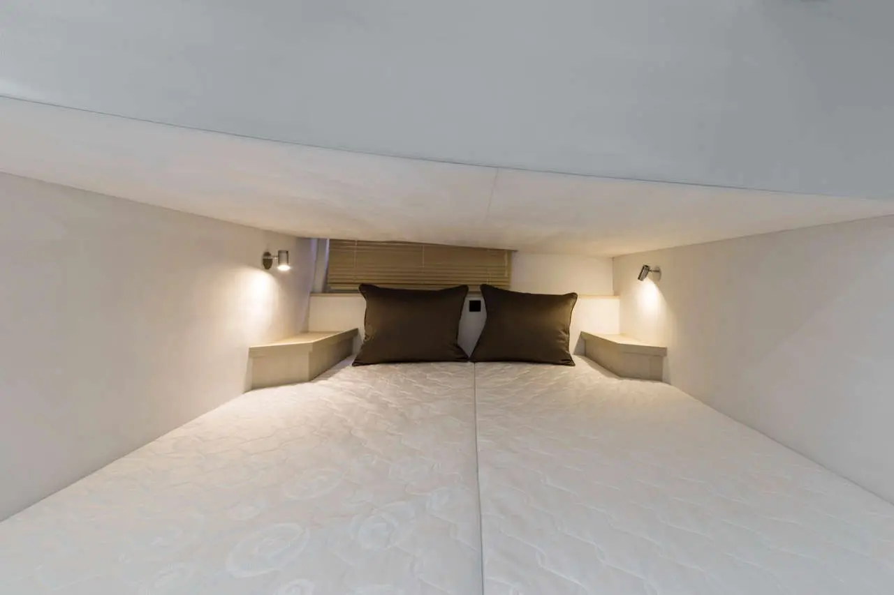 Cozy double bed with brown cushions, built-in bedside lights, and under-shelf storage in a compact, modern room interior.