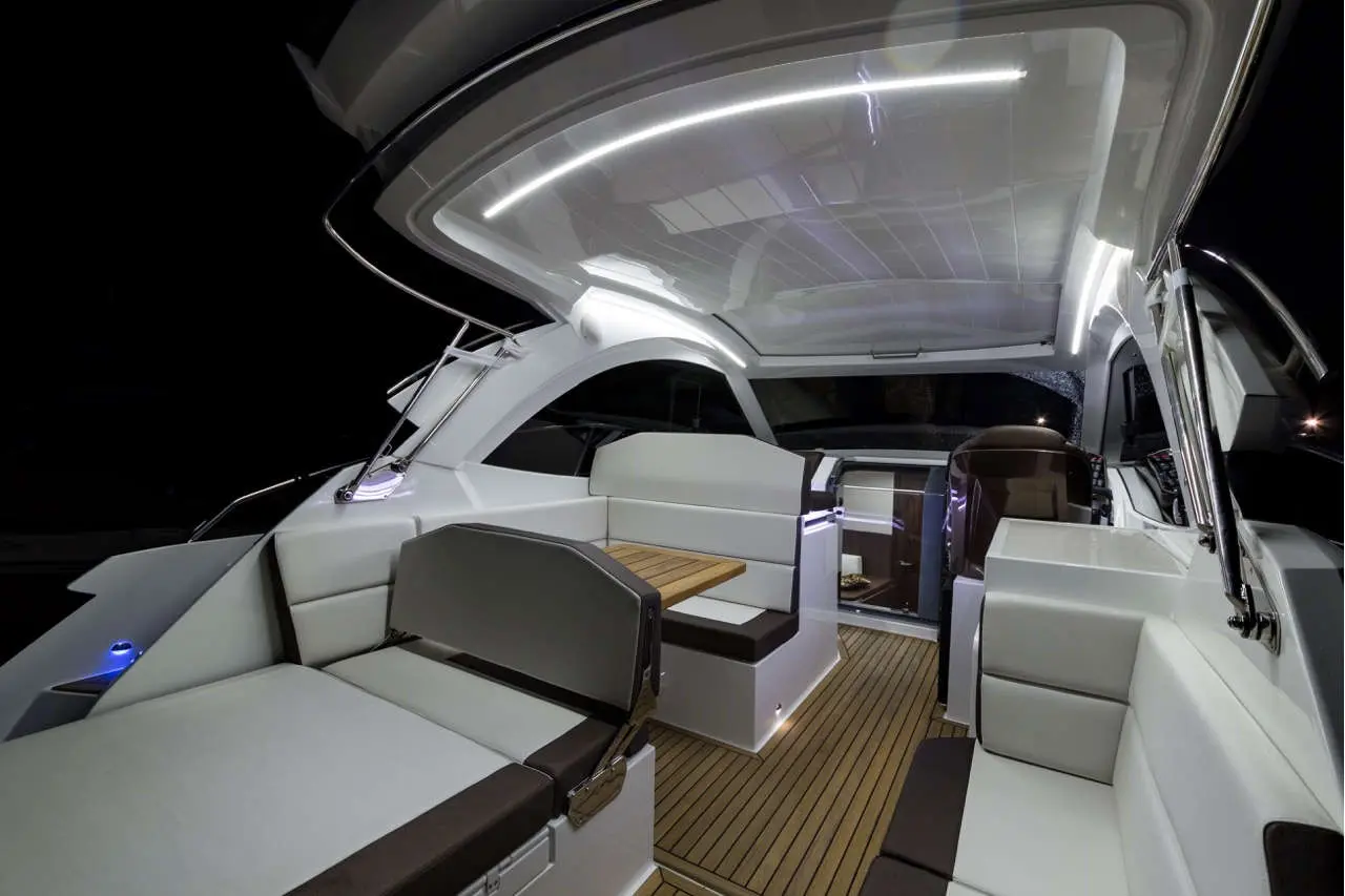 Modern boat interior at night, featuring sleek white and brown seating, a wooden table, and ambient lighting.