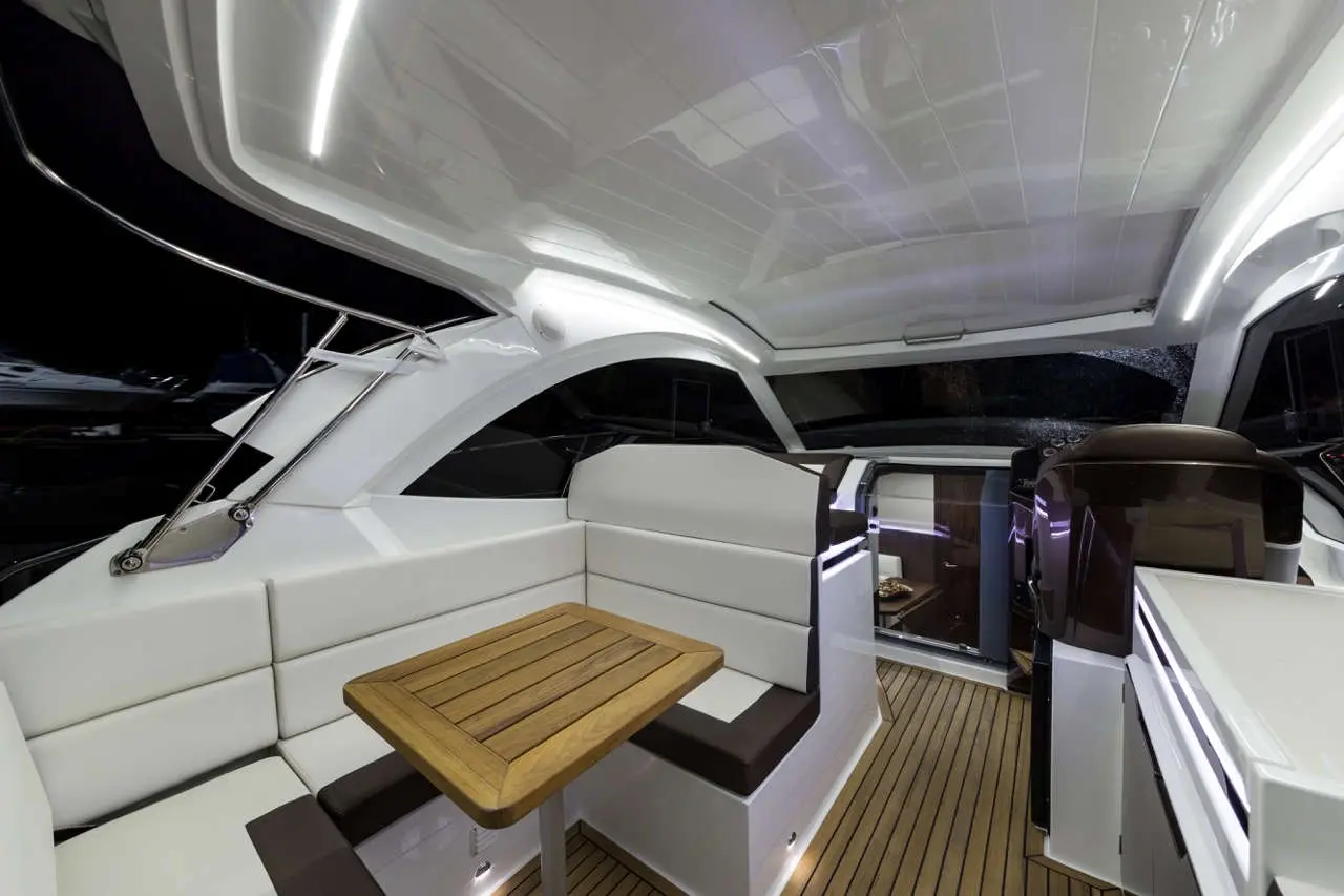 Sleek boat interior featuring white seating, a wooden table, and modern lighting, highlighting luxury marine design.
