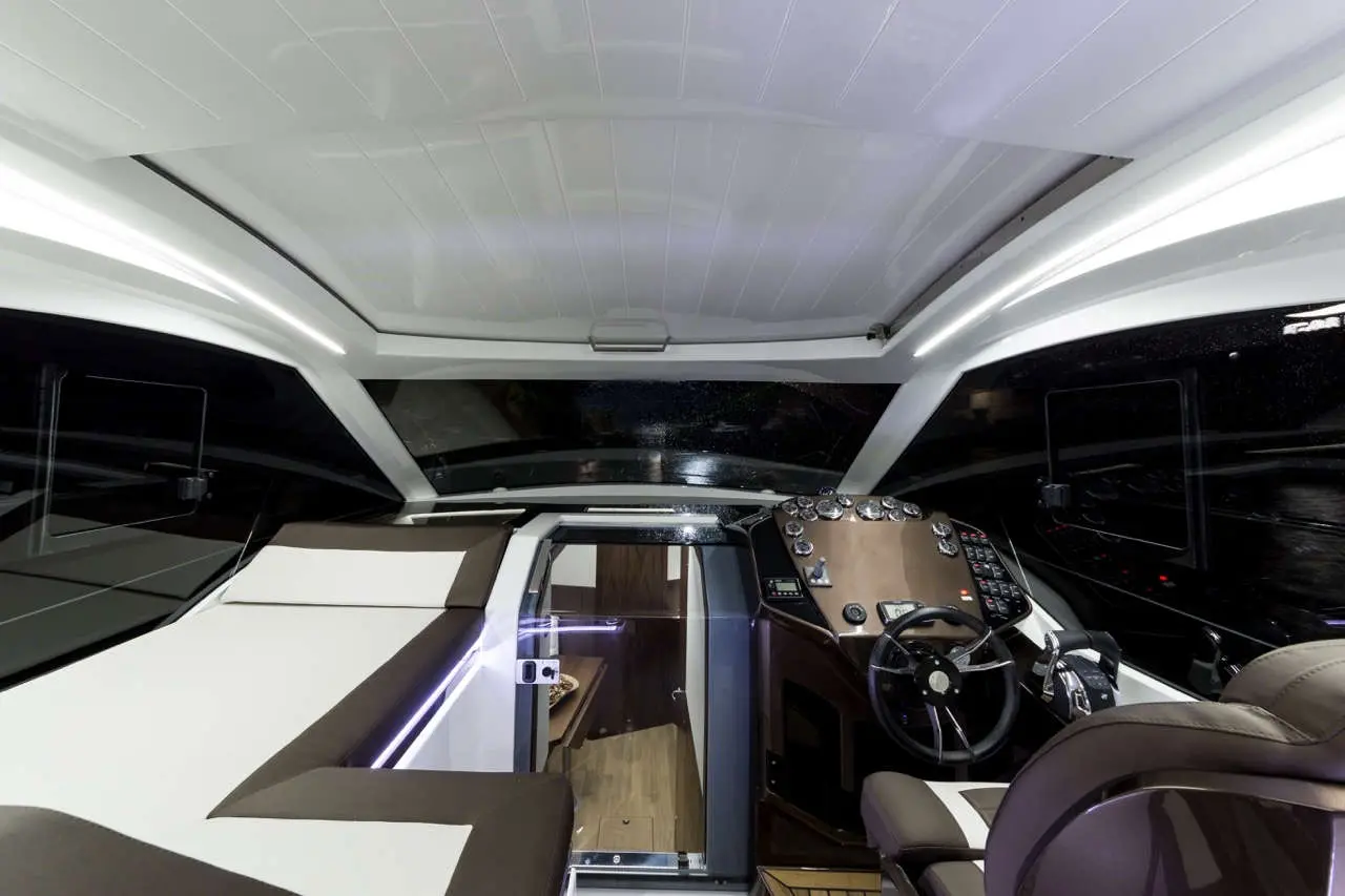 Interior view of a modern boat's control deck, featuring a steering wheel, dashboard, and comfortable seating area.