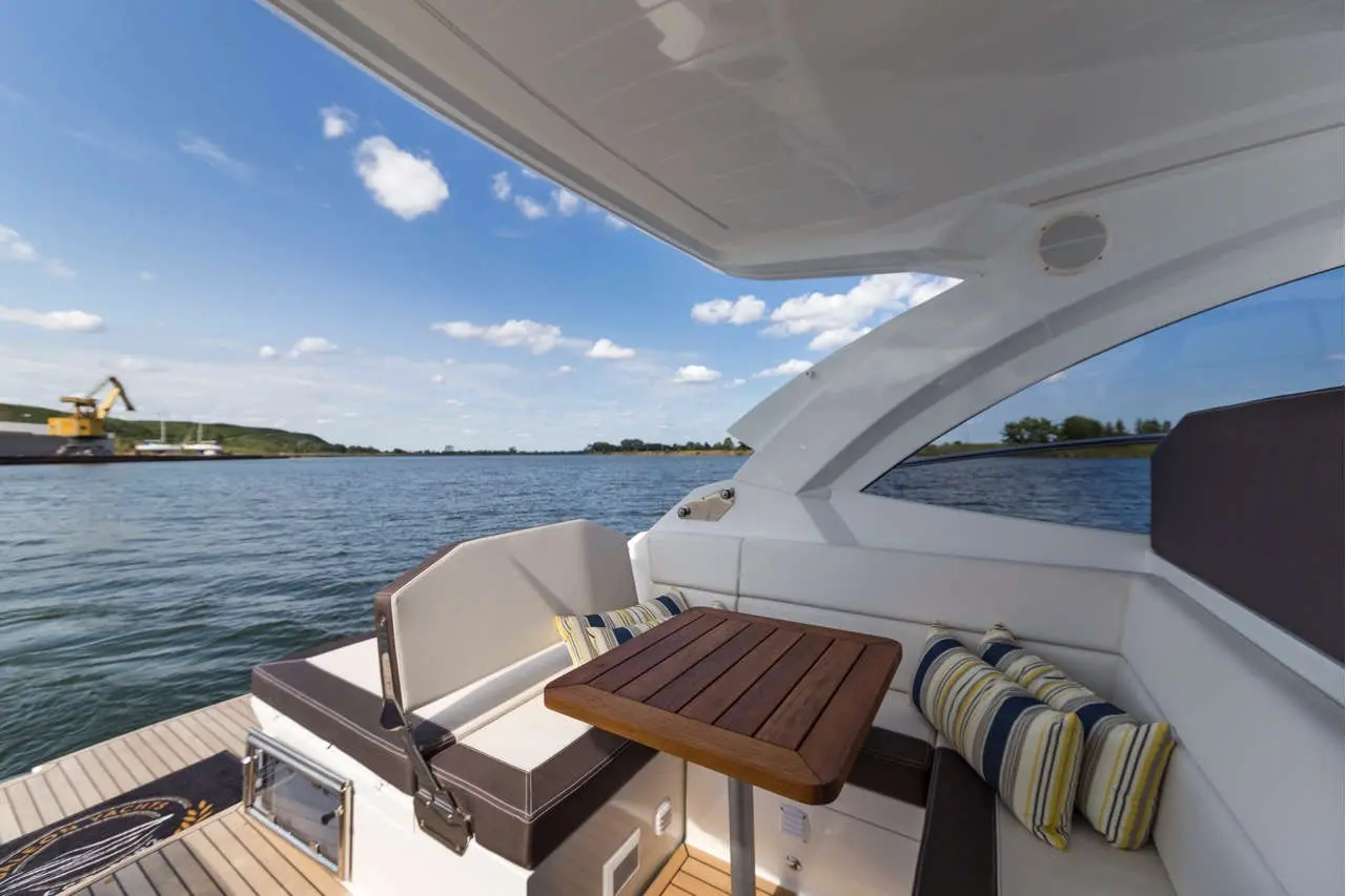 Luxury boat interior featuring a wooden table and striped cushions, with serene water and blue sky in the background.