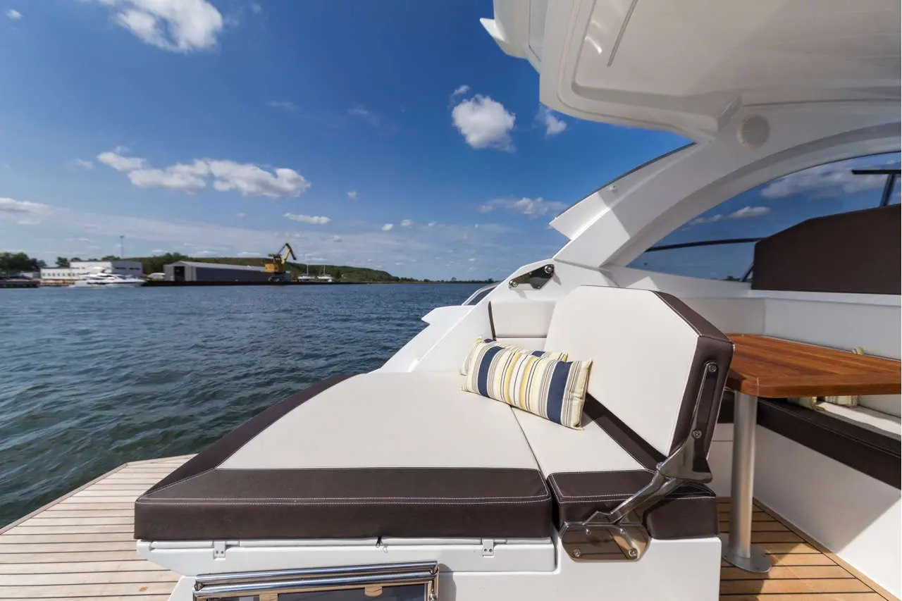 A sleek yacht deck featuring a cushioned seating area with a striped pillow, overlooking calm water and scenic boatyard.
