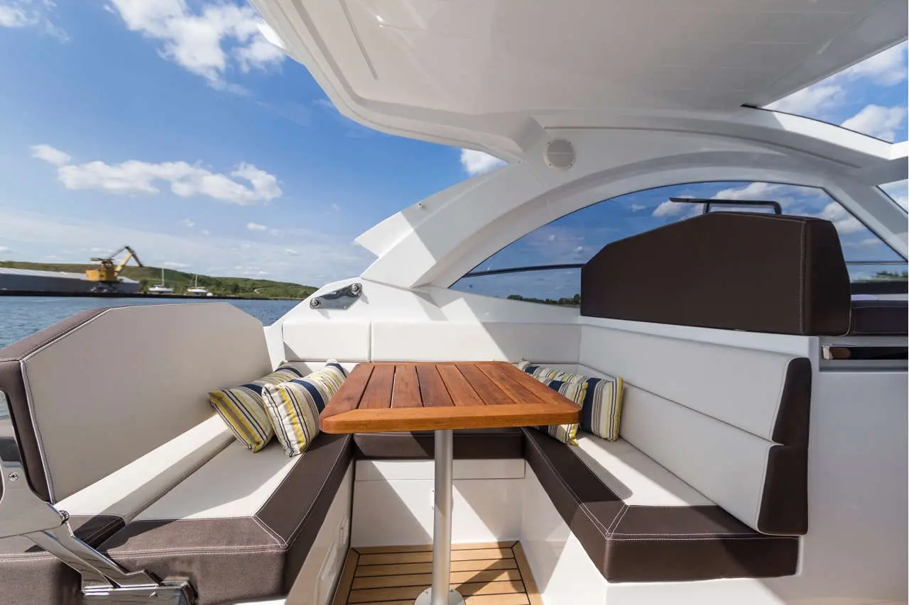 Luxury boat interior with plush seating, a wooden table, and striped cushions, showcasing scenic water views and blue skies.