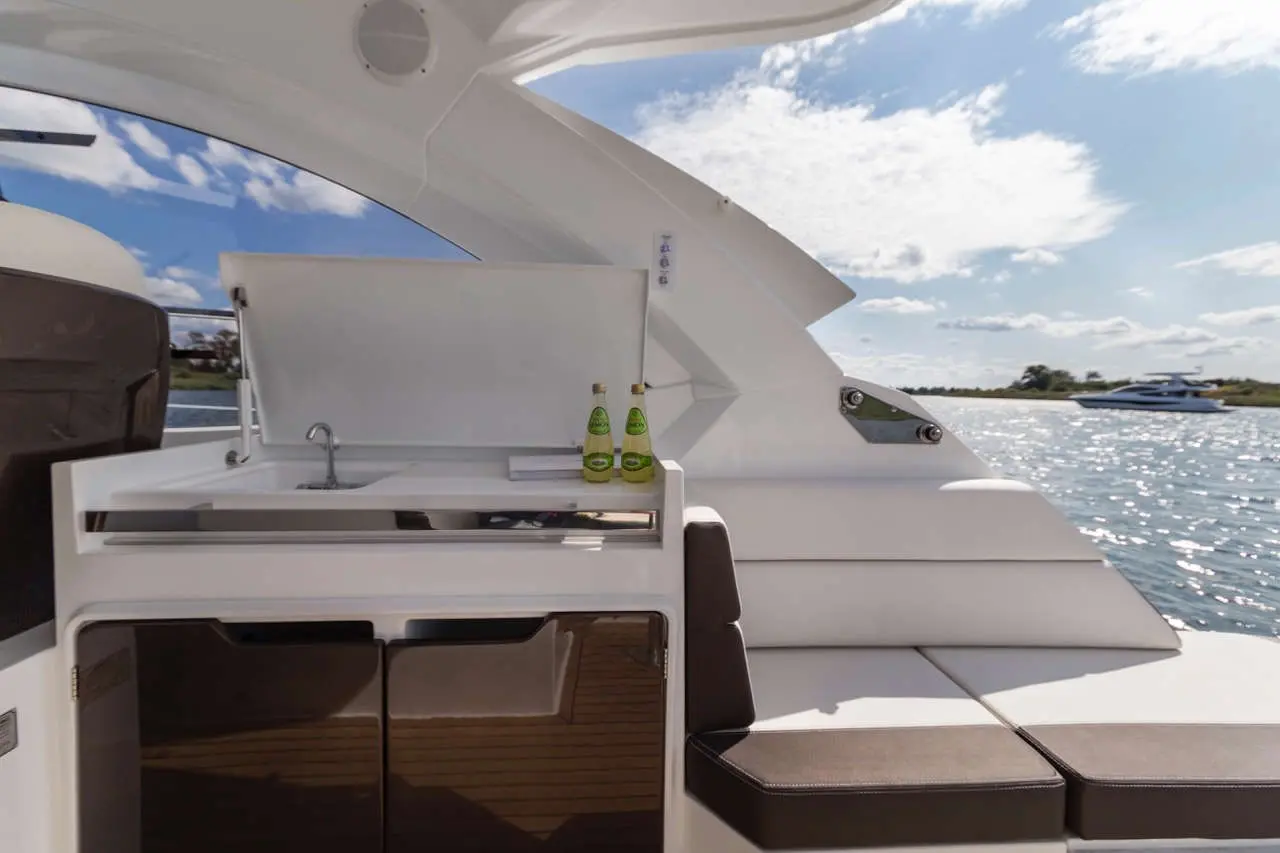 A modern yacht's cockpit features a sleek sink, drinks on display, and expansive views of the water and sky.