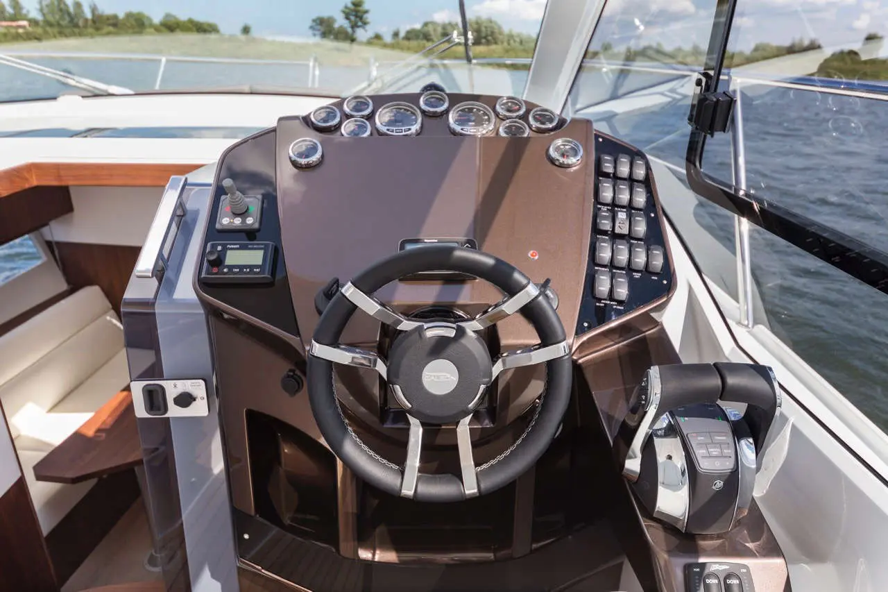 Boat dashboard featuring a steering wheel, gauges, control panel, and throttle, set against a water backdrop.