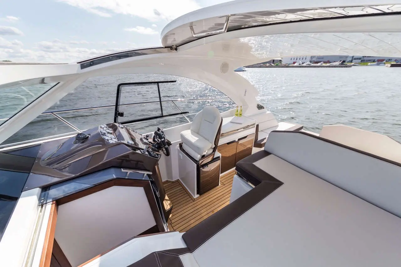 Modern yacht cockpit featuring a steering wheel, navigation controls, and luxurious seating with a view of the water.