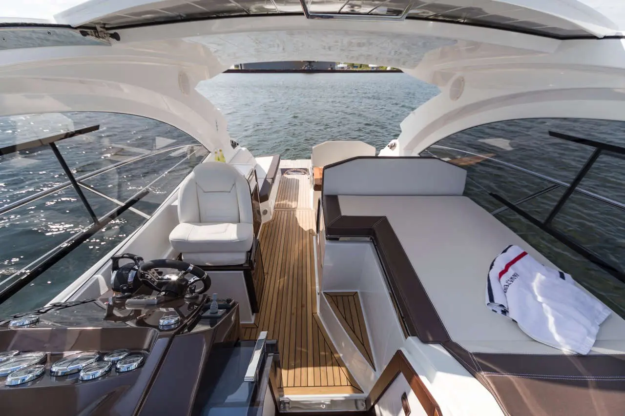Luxury yacht interior featuring a helm, comfortable seating, and views of the water, with a towel draped over a lounge.