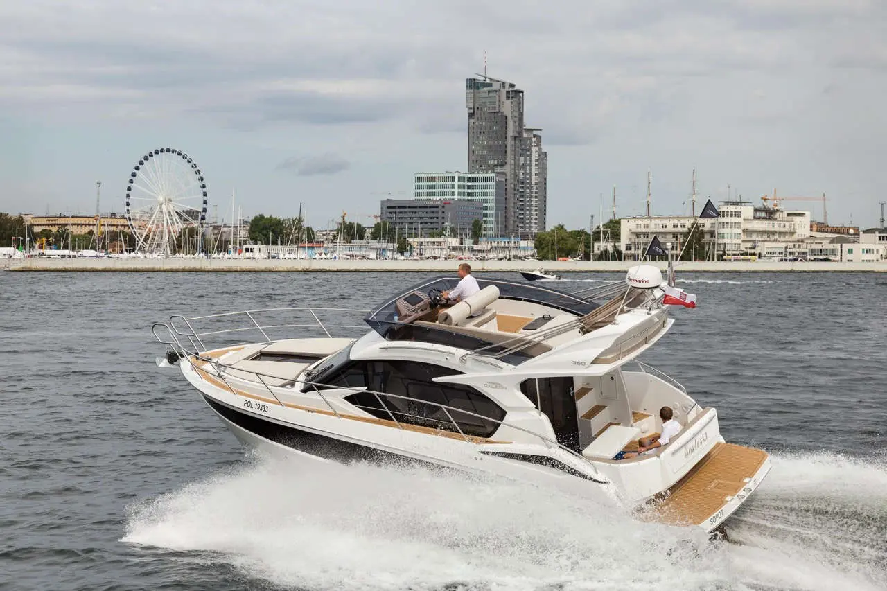 A motorboat with a man at the helm navigates through water near a city skyline and a ferris wheel.