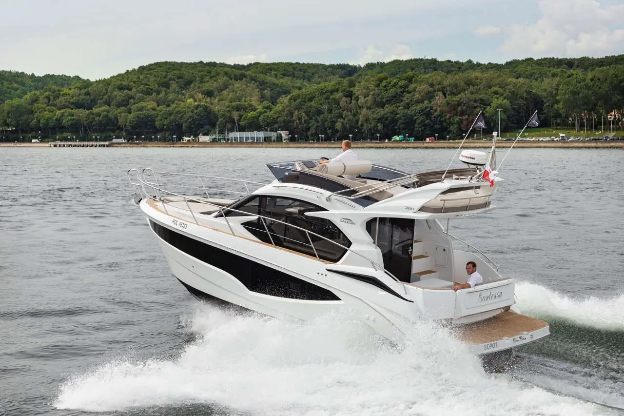 A sleek motor yacht, named 'Corletta', speeds through water with two men onboard, surrounded by greenery and a distant shore.