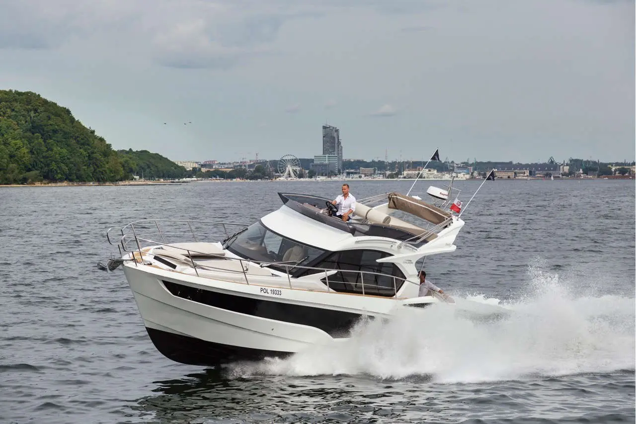 A luxury motorboat with a captain navigating on a lake, city skyline visible in the background, and splashes of water.