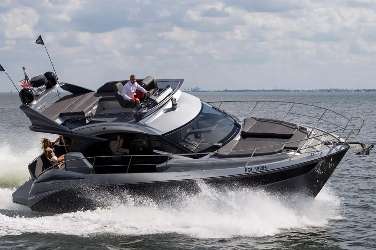 A sleek motorboat with a man at the helm and a woman enjoying the ride, ploughing through waves under a cloudy sky.