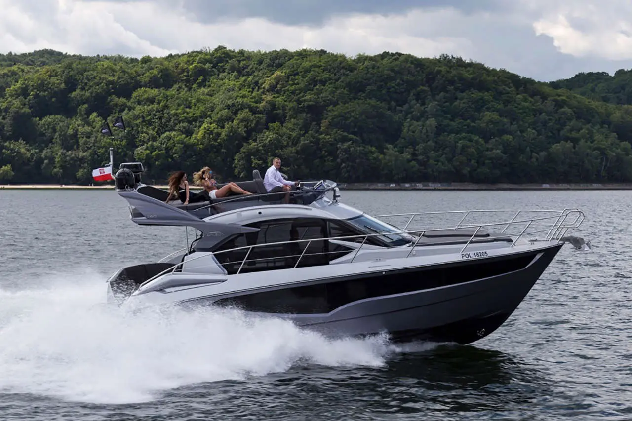 A sleek motorboat speeds across water, with three people aboard enjoying the ride against a lush green shoreline.