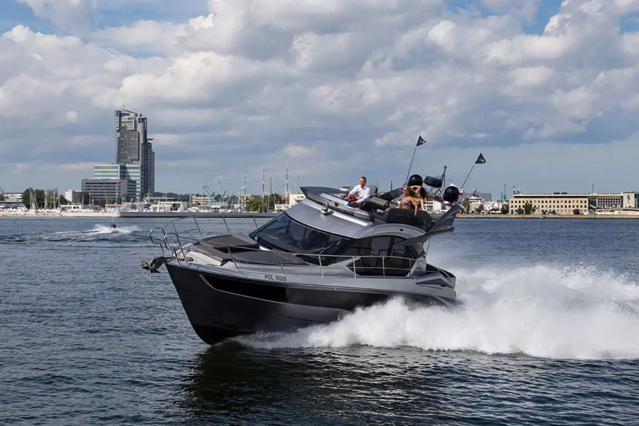 A sleek motorboat speeds across a river, with a city skyline in the background and passengers enjoying the ride.