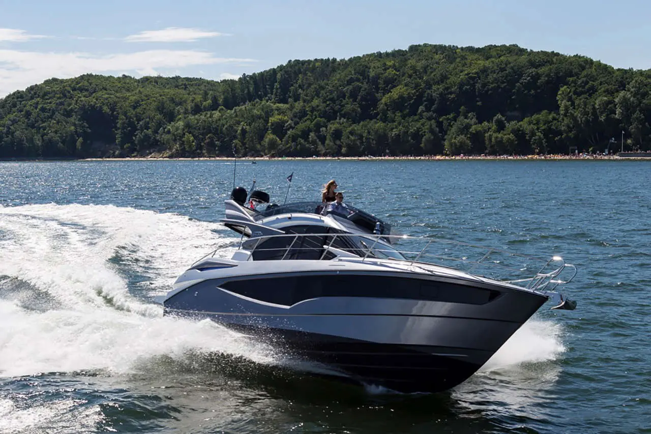 A sleek motorboat speeds across sparkling water with passengers enjoying a sunny day, surrounded by lush green hills.