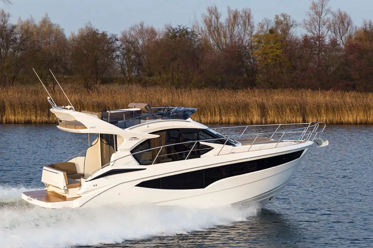A sleek white motorboat cruising on calm water with a backdrop of trees and reeds, showcasing a stylish design and speed.