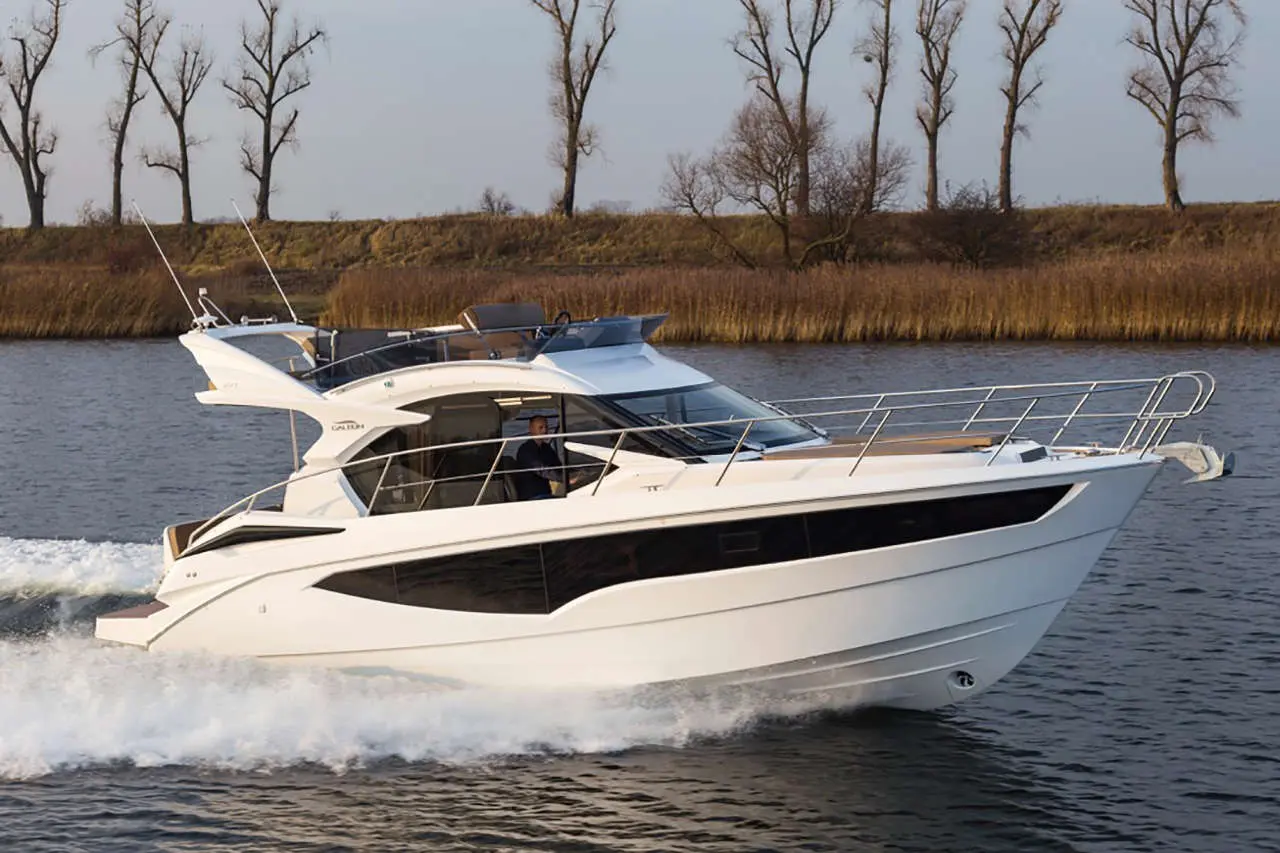 A sleek white motorboat cruising on calm waters, with a driver visible, surrounded by trees and marshland.