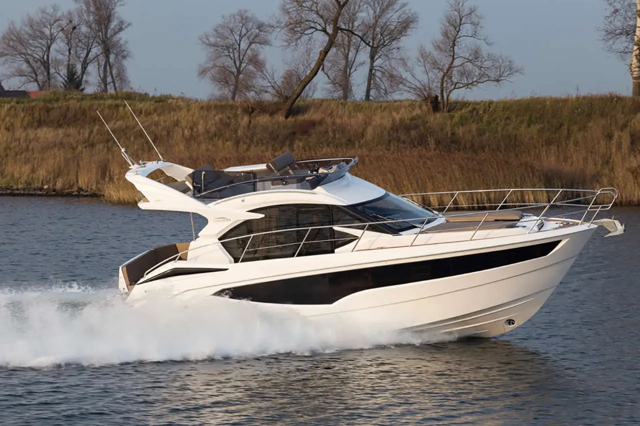 Luxury motor yacht cruising on water, showcasing modern design and sleek silhouette against a backdrop of trees and grass.