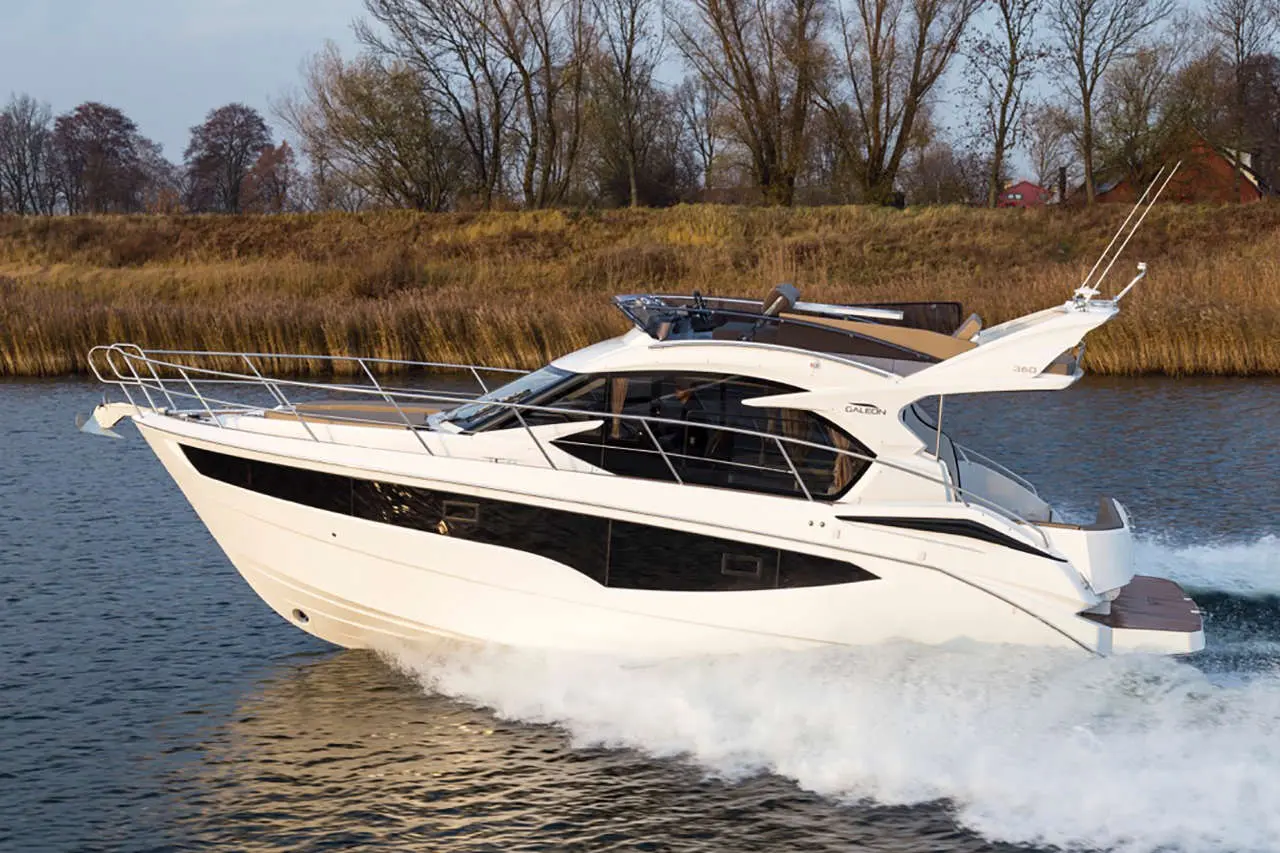 A sleek white motor yacht glides across the water, surrounded by trees and reeds, showcasing luxury and design.