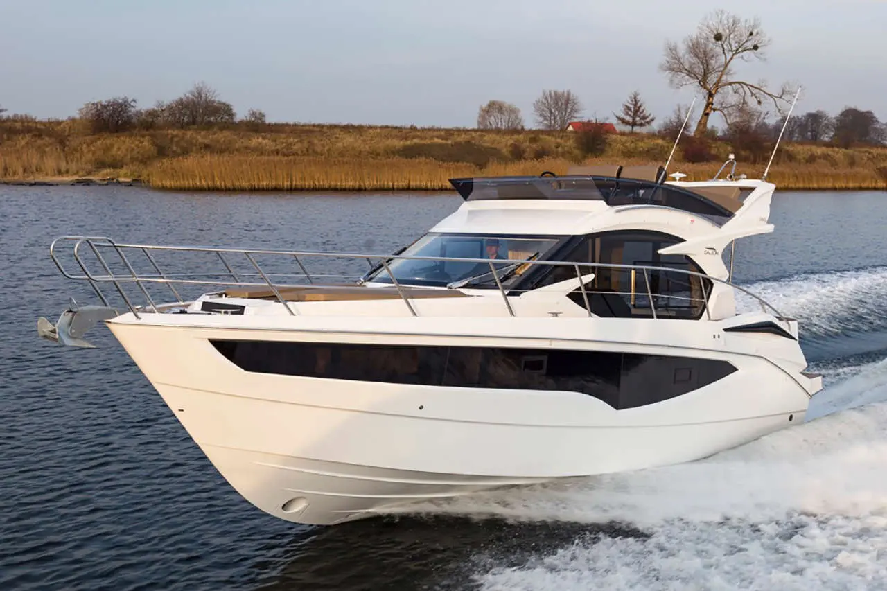 A sleek white motorboat cruises on calm waters, with a grassy shoreline and trees in the background, creating a scenic view.
