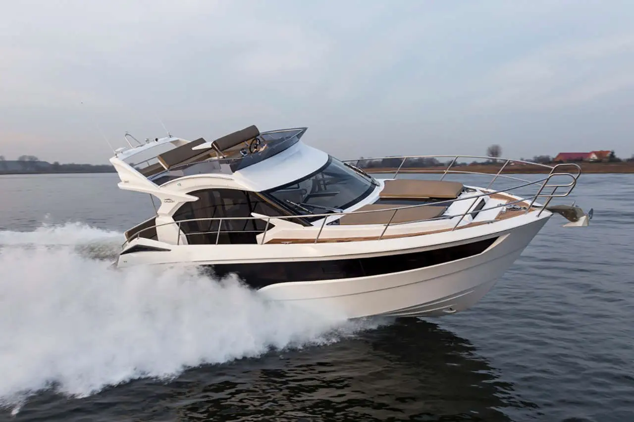 A white luxury boat speeds across calm waters, creating splashes as it navigates under a cloudy sky.