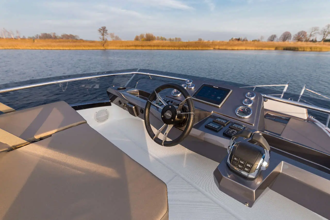 Boat cockpit view showcasing the steering wheel, control panel, and tranquil water scenery under a clear sky.