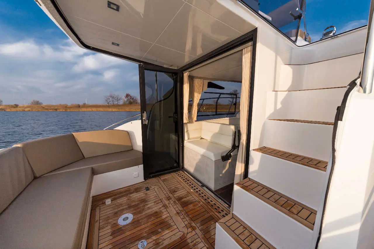 Interior of a boat showing stairs, leather seating area, and a view of water and greenery from the door.